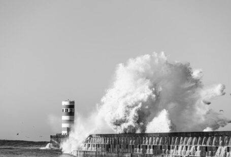 Coastal Resilience - a black and white photo of a large wave hitting a lighthouse